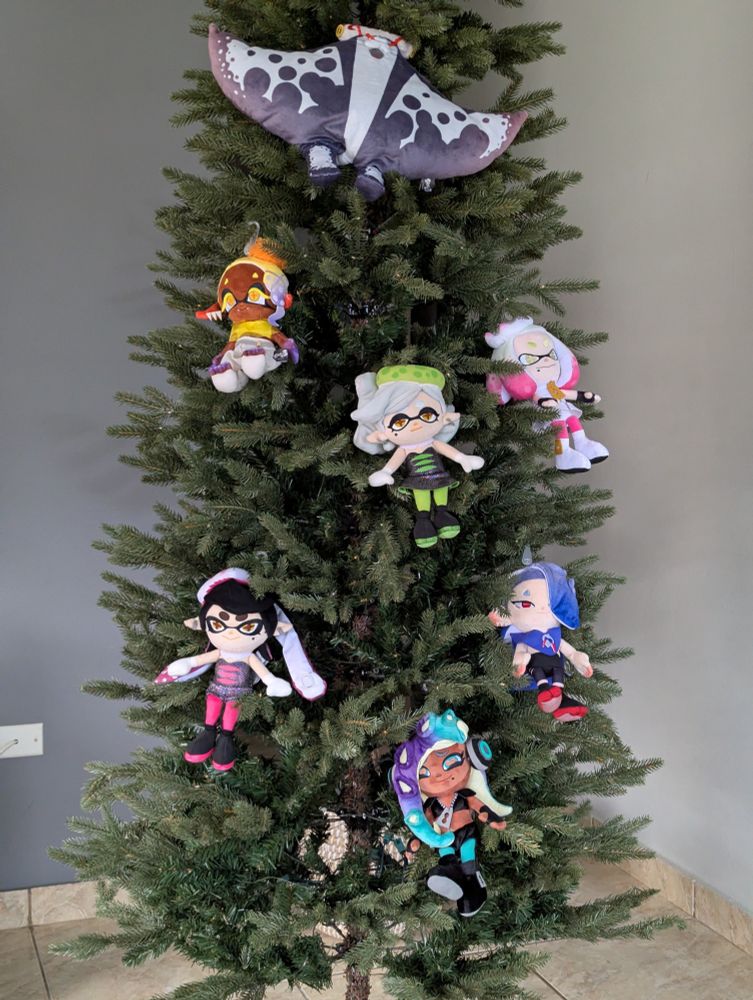 A Christmas tree decorated only with Splatoon idol plushies. Big Man Plush is hanging near the top, Frye Plush is below him and to the left, Pearl Plush at around the same height but on the right side, Marie Plush is in the center of the tree, Callie Plush is below and to the left, Shiver Plush is at the same height as her but on the right side, and Marina Plush is on the middle below the previous two.