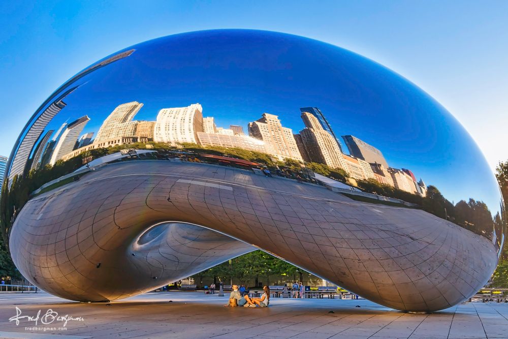 The Bean in Chicago reflecting the skyline in it's shiny chrome surface with a couple sitting underneath looking up into the Bean