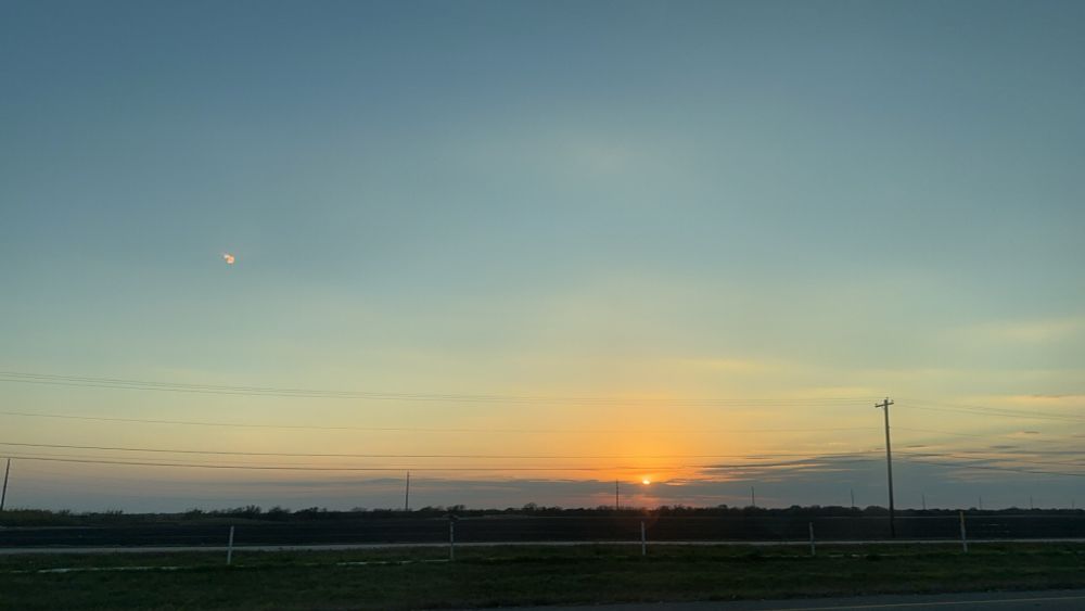 a sunset sky, with the sun just about to dip below the horizon. colors are warmer and there’s only some clouds close to the horizon. a telephone pole is seen on the right side 
