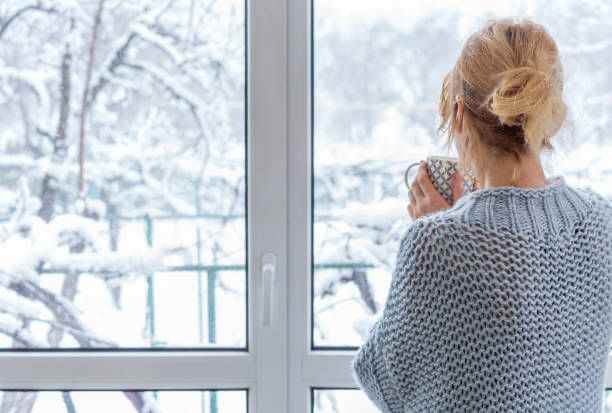 Stock photo of a lady staring out the window at snow