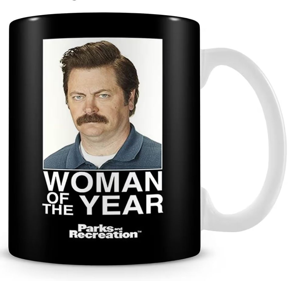 A black mug with a white handle with an image of Ron Swanson from the Parks and Recreations with the text: WOMAN OF THE YEAR

Parks and Recreation 