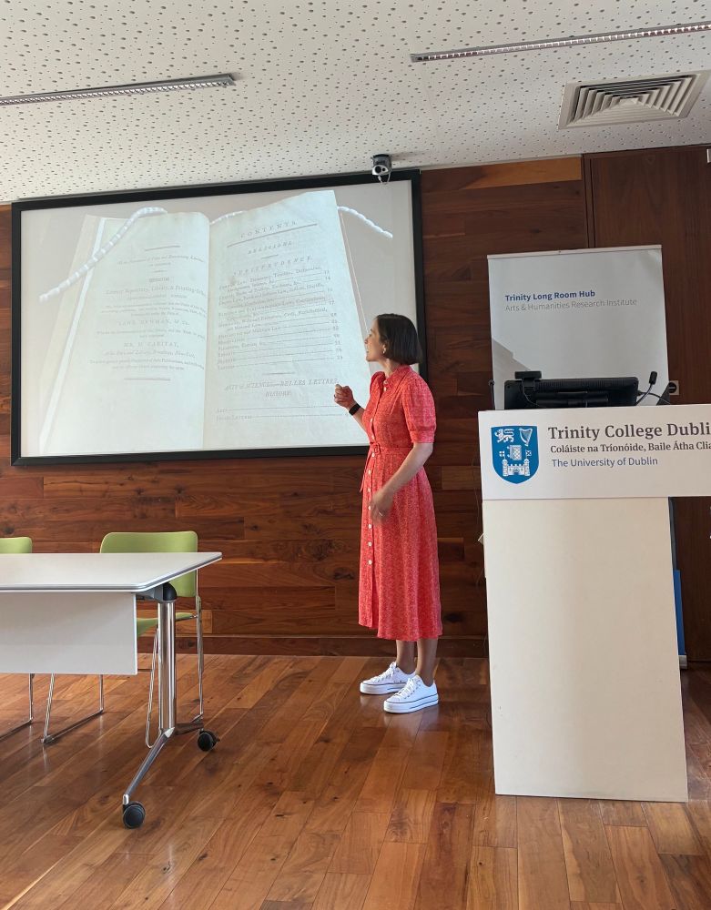Women in red dress and white runners points at a screen on which a book is displayed. 
