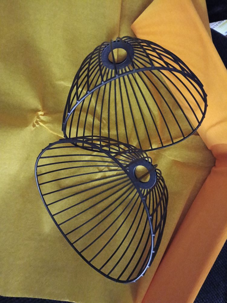 Two dome shaped black wire lampshades on a roll of orange crepe paper. 