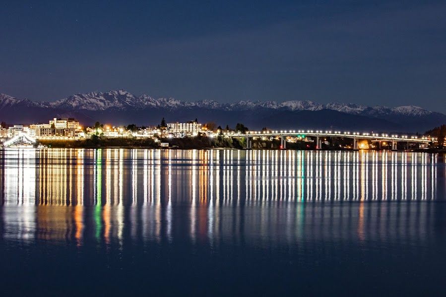 A mountain range and lights of a port city reflecting off the water