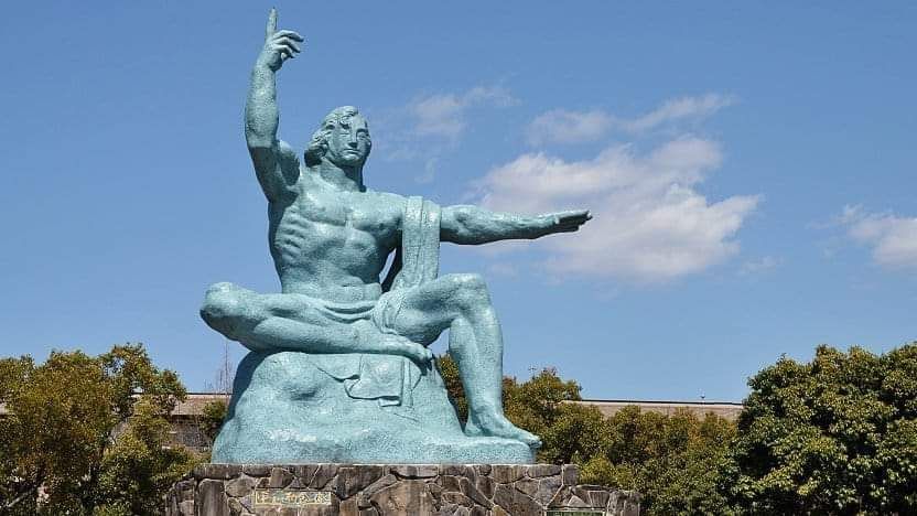 The Nagasaki Peace Statue, located in Nagasaki Peace Park, Japan is a powerful symbol of hope and a memorial for peace. It's a 9.7-meter-tall bronze statue created by Seibo Kitamura, a Nagasaki native. The statue's right hand points to the sky, representing the threat of nuclear weapons, while the extended left hand symbolizes eternal peace. The closed eyes convey a prayer for the souls of the war dead. 
Here's a more detailed breakdown of the statue's symbolism:
Right Hand: Points upward, symbolizing the threat of nuclear weapons and the atomic bomb. 
Left Hand: Extends outward, symbolizing eternal peace. 
Closed Eyes: Symbolize a prayer for the souls of the atomic bomb victims. 
Overall: The statue embodies a universal prayer for world peace and a reminder of the tragic consequences of war. 
The statue was unveiled on August 9, 1955, the tenth anniversary of the atomic bombing of Nagasaki. The park itself was built on a low hill north of the atomic bomb's hypocenter, representing the wish for world peace and a vow that such a tragedy would never be repeated, says www.discover-nagasaki.com. 
