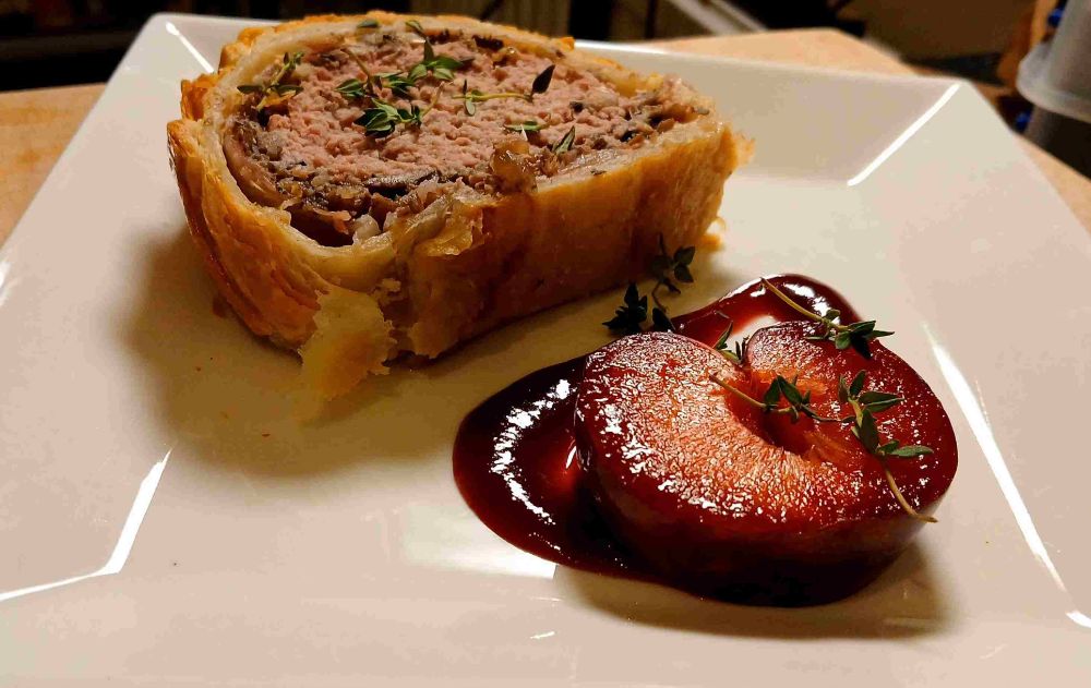 Smoked duck wellington with a boozy plum sauce and a half a plum garnish. closeup shot