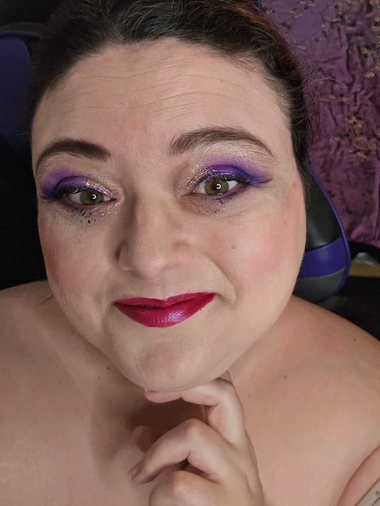 Woman smiles at camera. Wearing purple eyeshadow and red lipstick