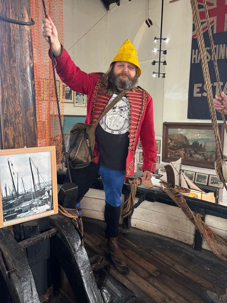 Picture of a twat in blue-and-black quartered jeans, a red coat, and a yellow hat. 