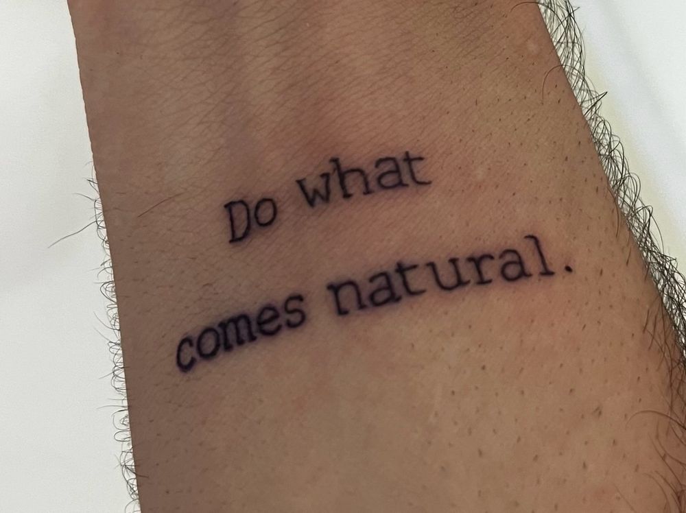 Inked letters on the right arm that say "Do what comes natural."
