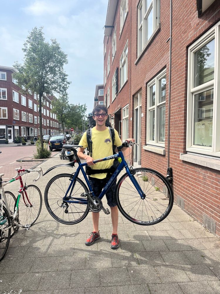 Photo of me holding a blue super cool and shiny bike, on the sidewalk of a street.