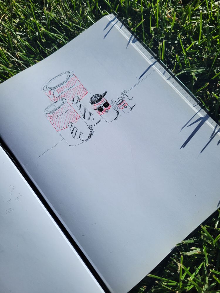Sketchbook laying in the grass opened up to a drawing of a homonorm family of Campbell's soup cans, where one of them is "cool" because it's wearing sunglasses and a sideways baseball cap