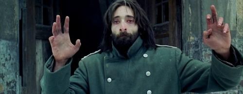 An emaciated Adrien Brody stumbles out of a crumbling building wearing a German officer's coat.