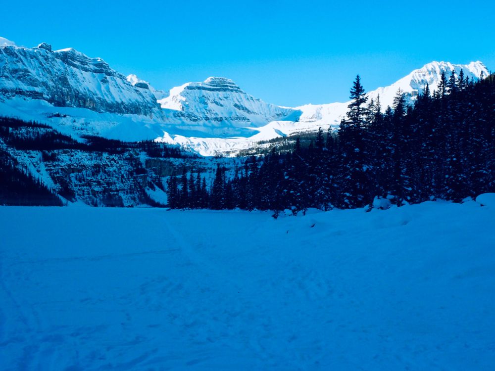 In front there is a frozen lake, already in the shade. The sun is still 
on the mountains behind topped by a blue sky without any clouds.