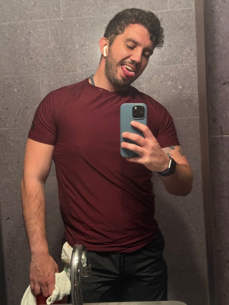 Nathan st the gym in his workout gear looking at his phone and sticking tongue out 