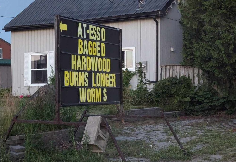 A sign that reads "at-esso bagged hardwood burns longer worms" where each word, except "burns longer", is on its own line