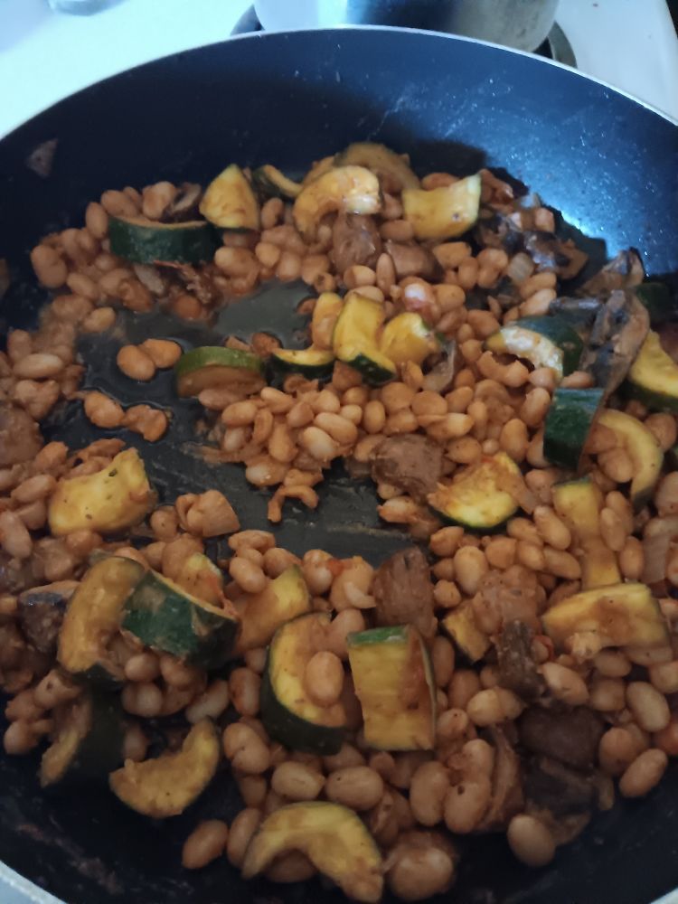 A frying pan full of mayocoba beans, zucchini halves, baby bella mushrooms, tomatoes, and onions.
