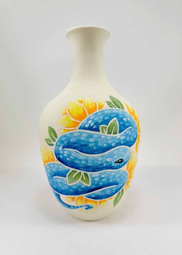 A handmade porcelain vase with an illustration of a blue snake on it.
