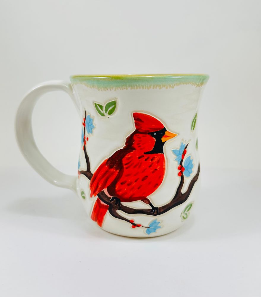 A handmade ceramic mug with an illustration of a cardinal on it. The mug is glazed in white on the outside and green on the inside. 