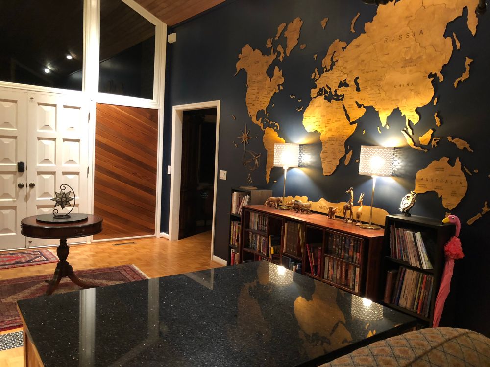 A wooden map adorns a navy blue wall, over a large bookcase. 
