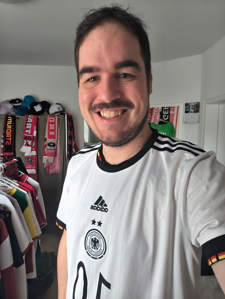 Ein Selfie im Deutschlandtrikot der Frauen  neben einem Kleiderständer mit anderen Trikots. Im Hintergrund hängen mehrere Schals