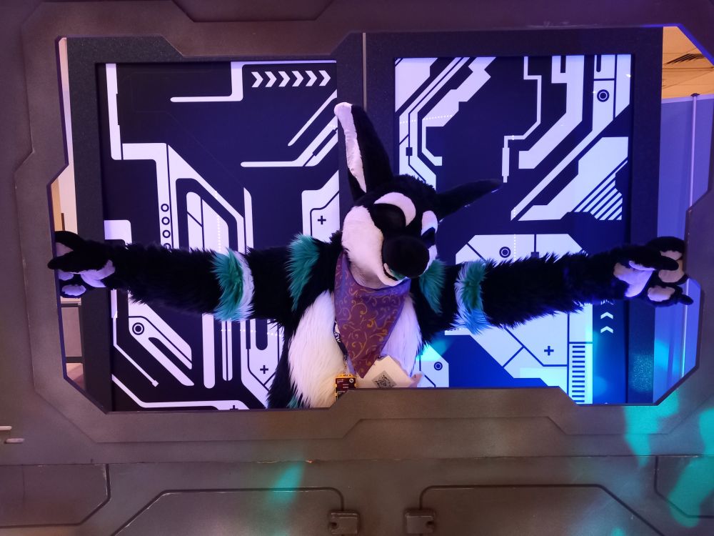 shedd the manokit fursuit at confuzzled 2025 posing with open arms with a tech themed background prop