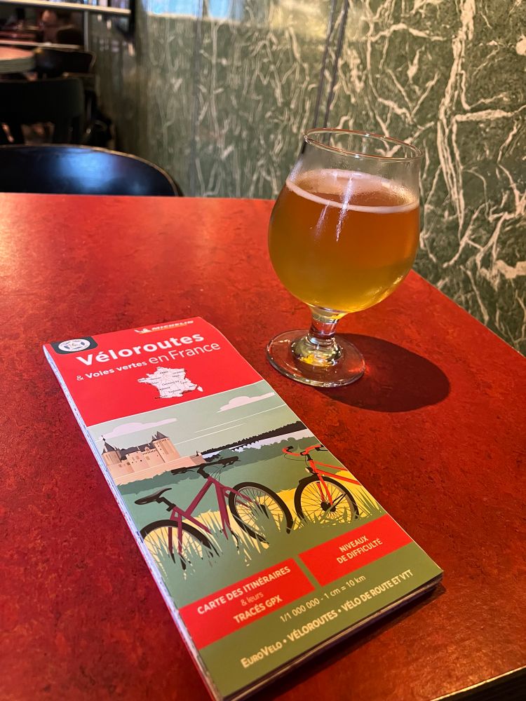 A photo of a cycling map of France on a table beside a glass of beer on a table in a bar. 