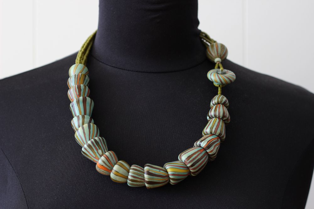 25” necklace of blown glass beads which nestle into each other with variegated stripe patterns that coordinate pleasingly in an ocean/coastal inspired color way. The blown glass disc is used as a button clasp and there are six strands of Czech glass seed beads to comfortably rest on the back of the neck or can be turned asymmetrical. Beads have been tumble etched to take away shine. All glass beads are made in my home studio and properly kiln annealed. 