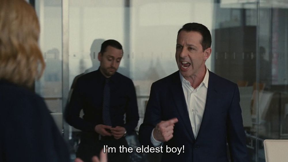 Scene from Succession where Kendell Roy is screaming at Shiv that he's the eldest boy while roman sulks in the background. 