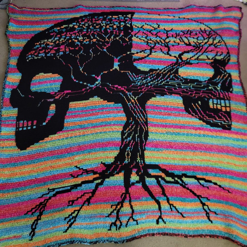 A mosaic crochet blanket of a tree that becomes skulls