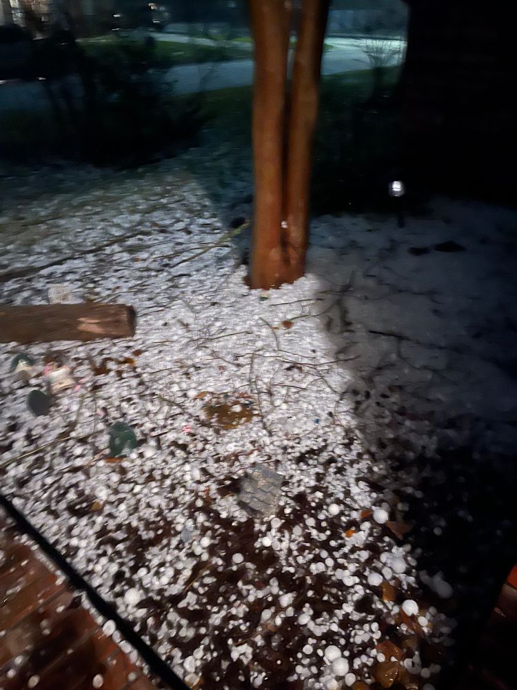 Ground outside house lit by porch light covered in large hail.