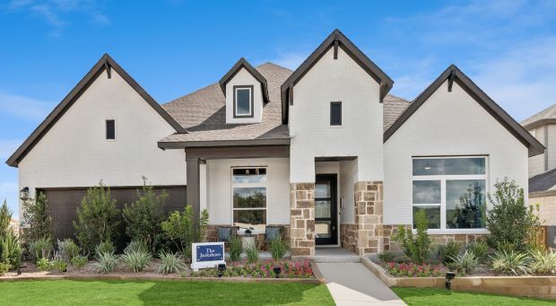 A modern single-story house with a white facade, large windows, and a landscaped front yard. The Jacksboro model home from David Weekly Homes is available to tour at the grand opening celebration in Windsong.