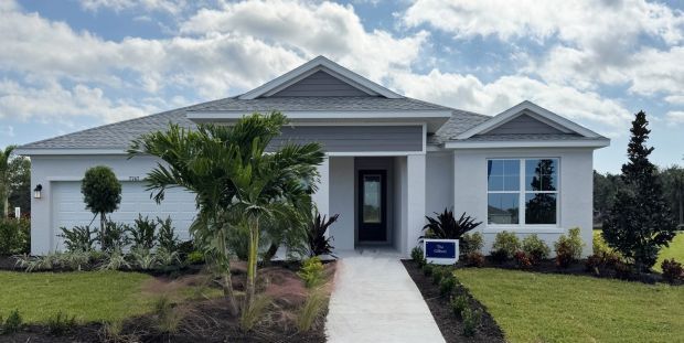 A modern single-story house with a neatly landscaped yard under a partly cloudy sky. The Gilbert model home from David Weekley Homes is now open for tours in Coasterra. 