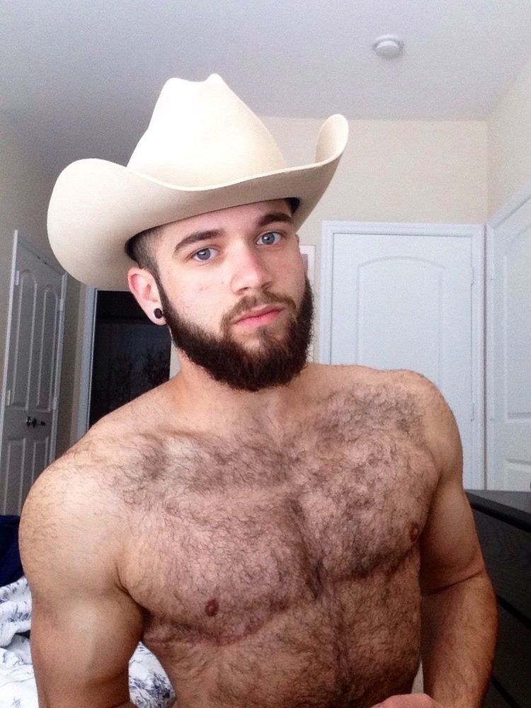 Hairy bearded trans man wearing a cowboy hat.