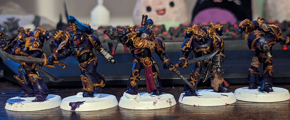 A photo of 5 Warhammer 40,000 miniatures painted in purple with gold trim