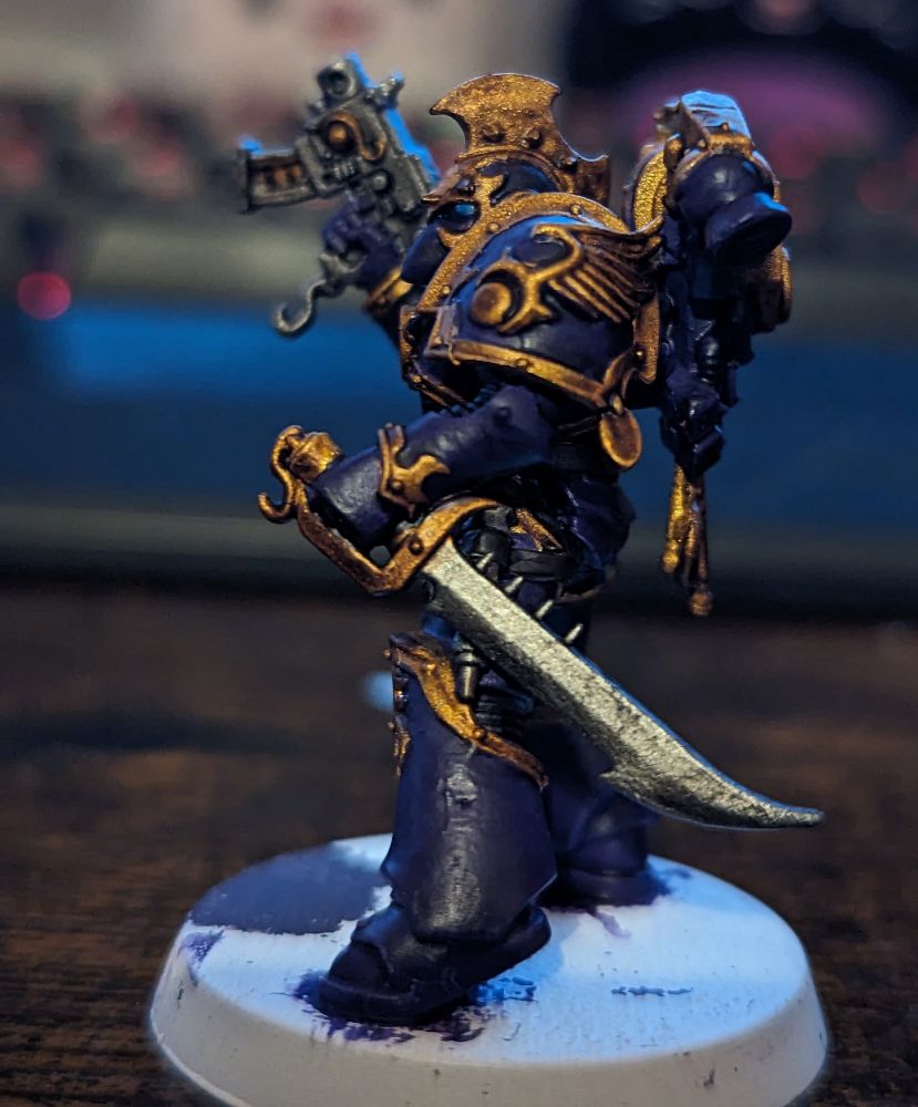 A Warhammer 40,000 miniature painted in purple armour with gold trim