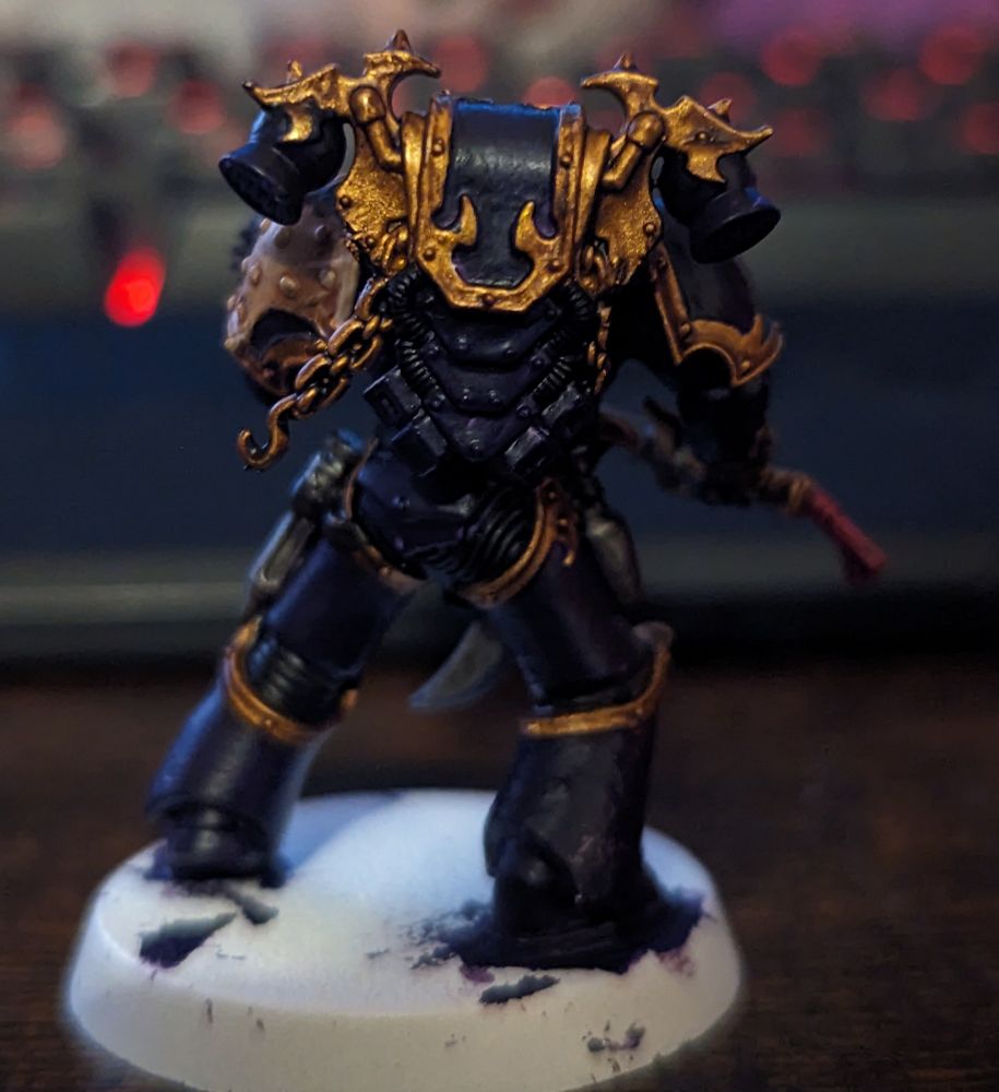 A Warhammer 40,000 miniature painted in purple with gold trim wielding a pistol and sword