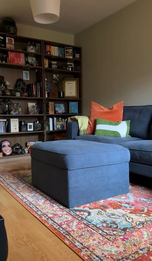 Cosy navy sofa next to a large wooden bookshelf on a red printed rug