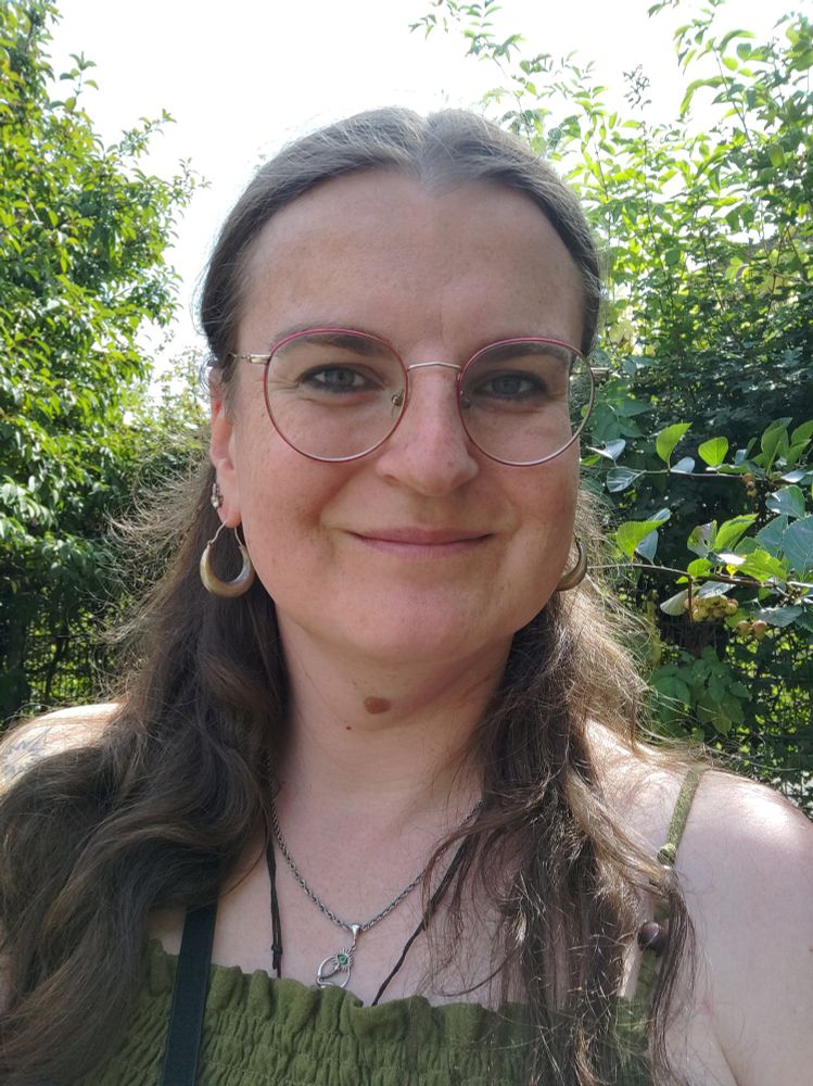 A vaguely smiling woman in between leavy greenery.