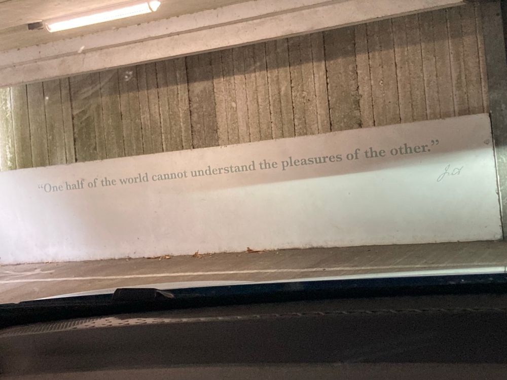 Shows a concrete walk in a car park with a type written quote on it “one half of the world cannot understand the pleasures of the other” J.A. 