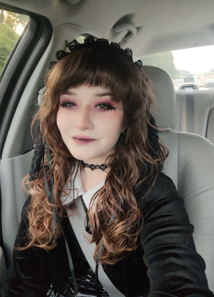 Goth girl with wavy brown hair and red eye makeup taking a selfie in a car