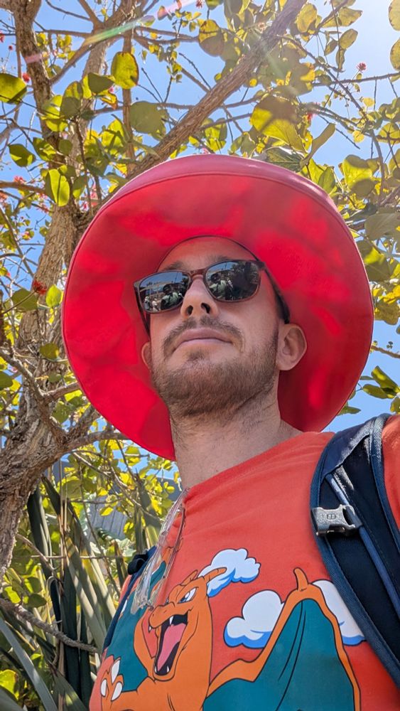 A selfie. I am wearing a pink sunhat, orange sunglasses, and a red Pokemon tshirt. 