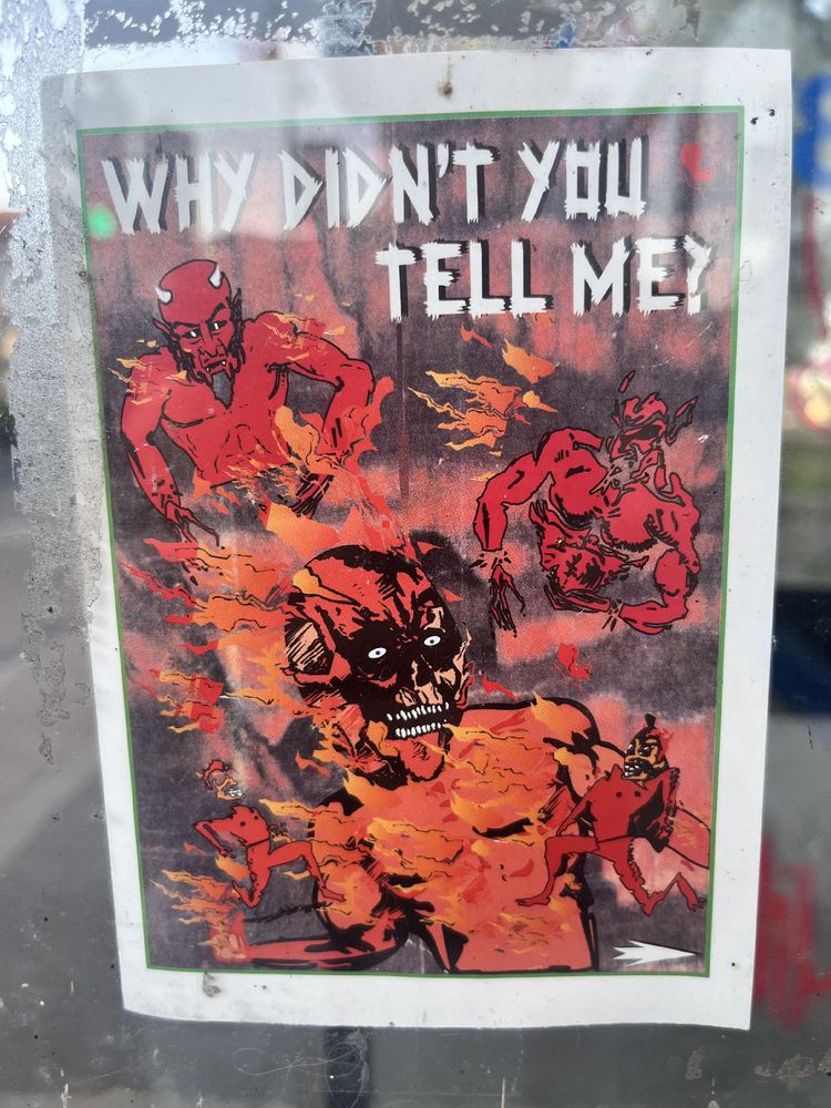 A poster showing (presumedly) demons screaming in Hell with the legend: WHY DIDNT YOU TELL ME?  - it is pasted onto a telephone box 