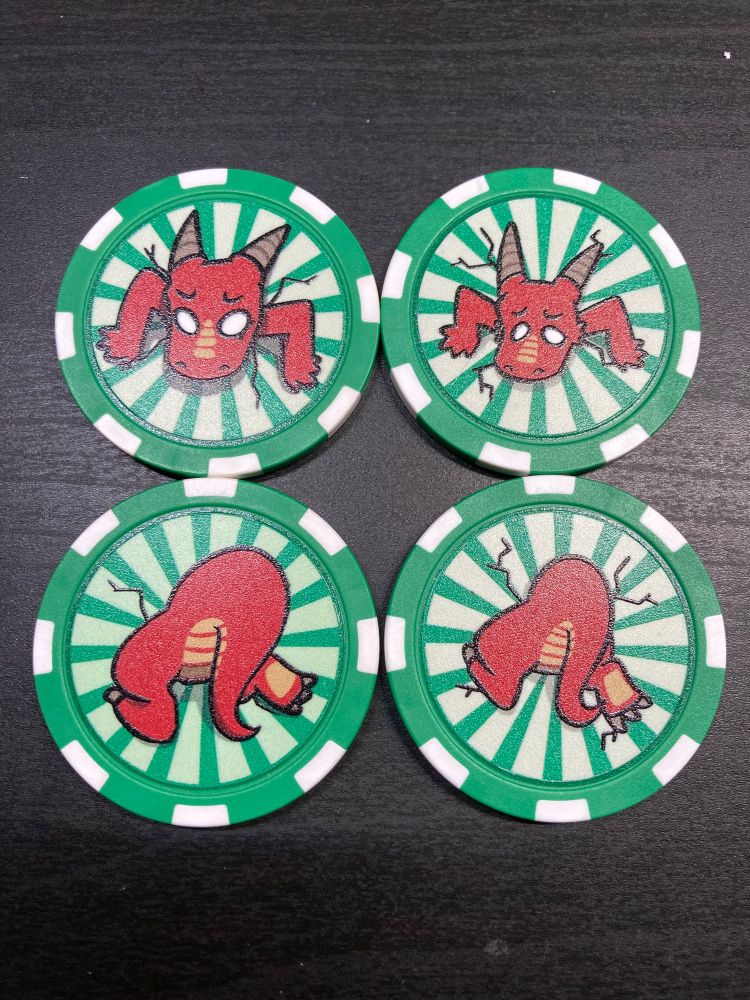 A photo of four green poker chips. They have a kobold/dragon stuck in them, one side has the face and the other the butt. The designs on the left are a little bigger than the ones on the right.