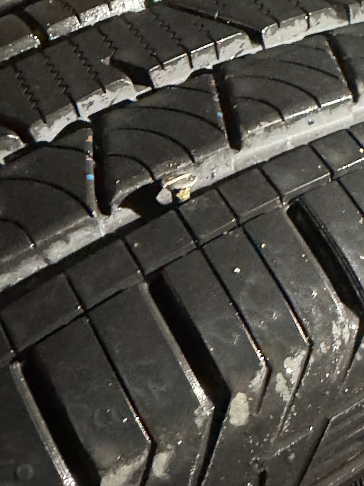 A new car tire with a large nail embedded in it 
