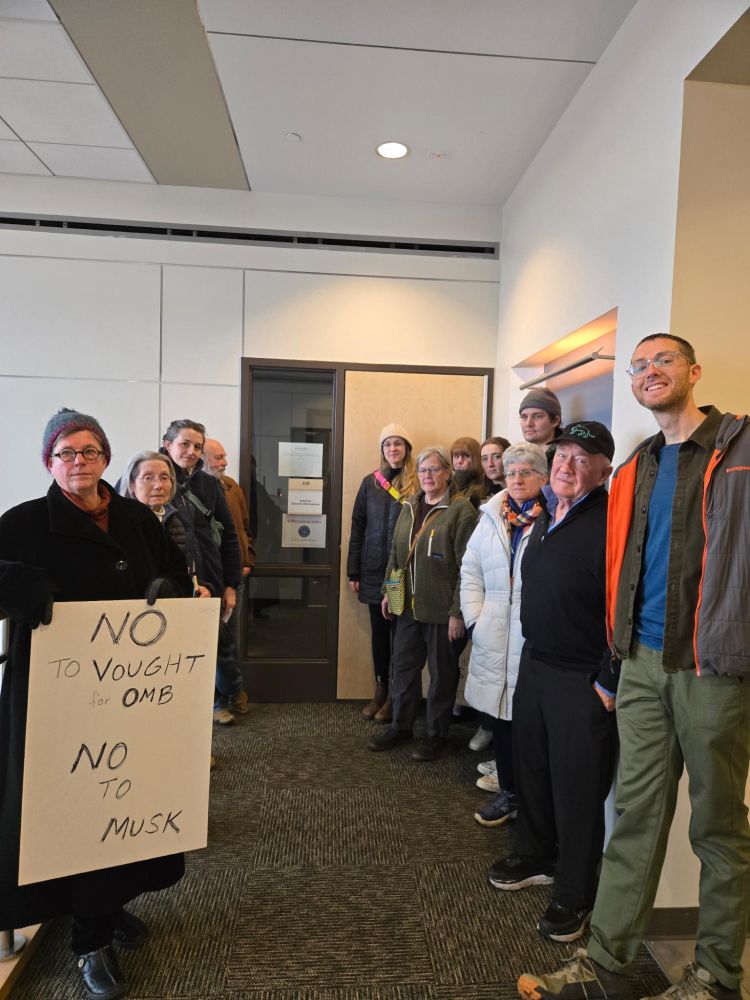 A group of people standing outside a closed office. One person is holding a sign.