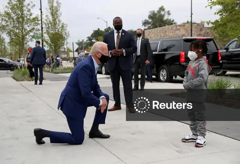 A picture of former President Joe Biden, kneeling as he speaks face to face with a child.