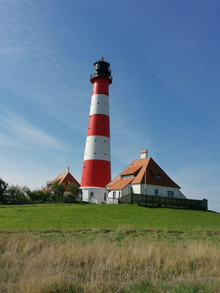Rotweiß geringelter Leuchtturm zwischen zwei Häusern und blauer Himmel