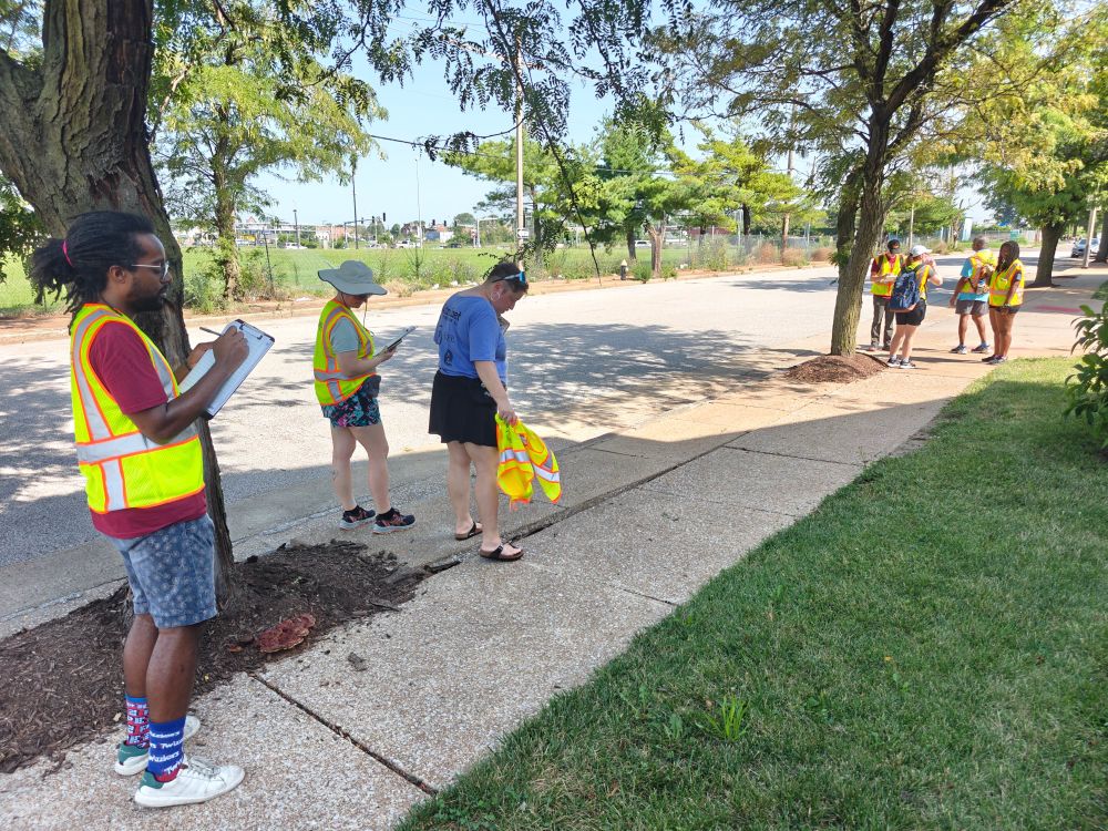 Trailnet staff members in hi-vis vests observing uneven sidewalks and taking notes as part of a walk audit. 