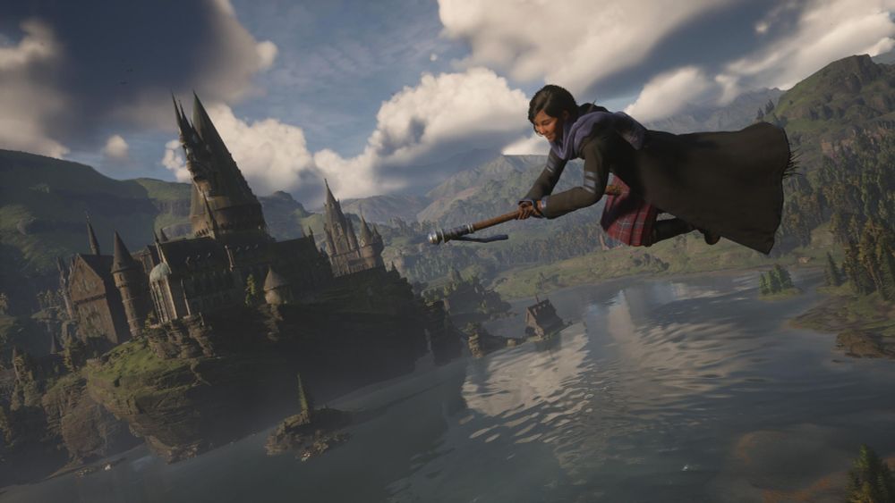 A screenshot from Hogwarts Legacy. A student flies on a broomstick with Hogwarts castle in the background.