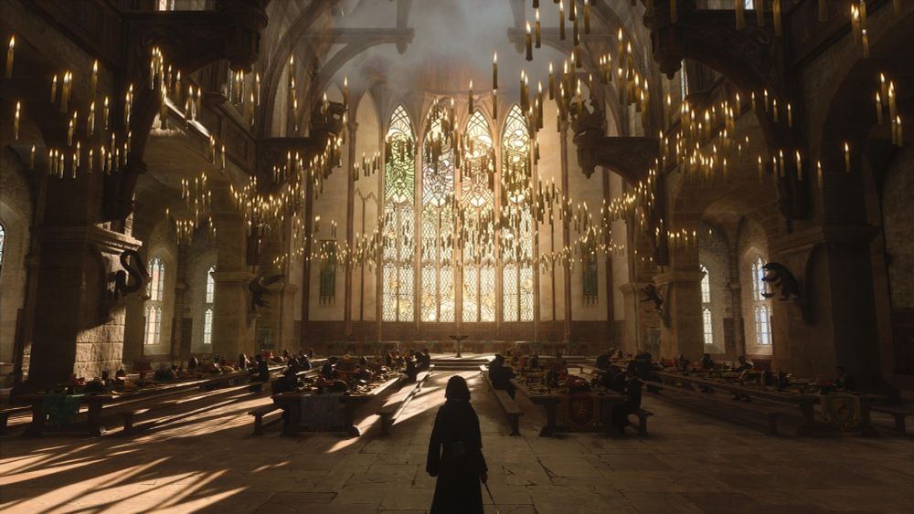 A screenshot from Hogwarts Legacy. A student stands in the middle of the Great Hall, with hundreds of candles floating near the ceiling. 